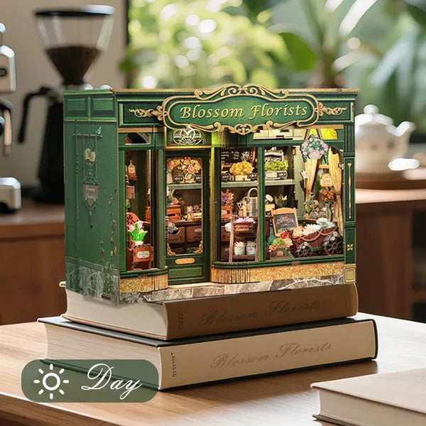 DIY Blossom Florists book nook kit on a wooden desk stacked on two books, daytime lighting showing the green exterior