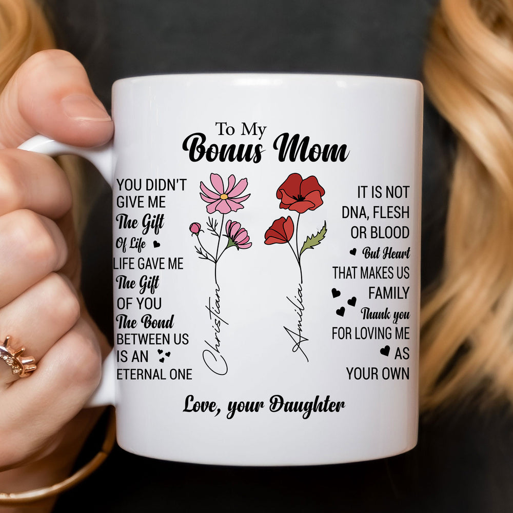 Close-up of hands holding a custom bonus mom coffee mug featuring sentimental text and family birth flowers.
