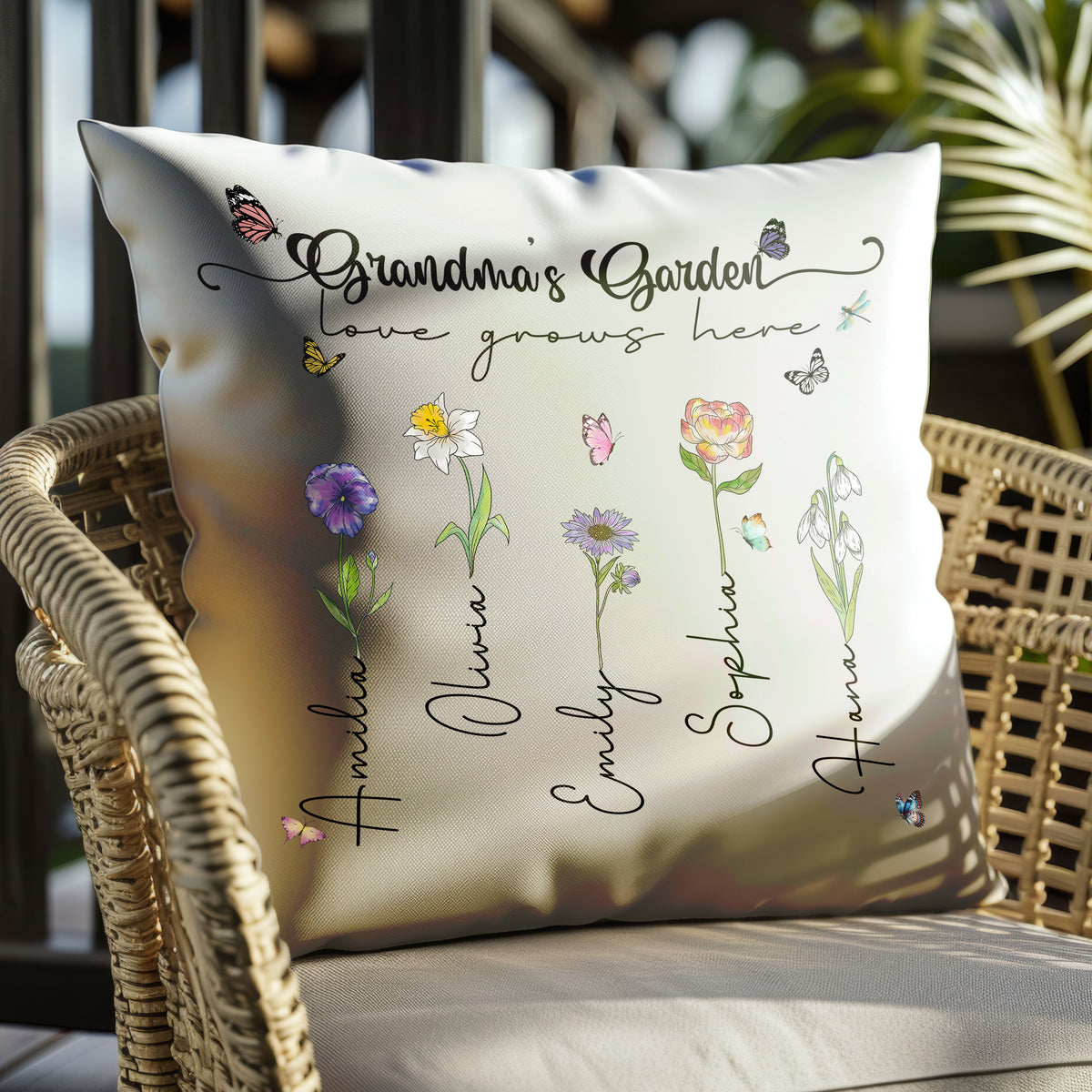 White Grandma's Garden pillow with watercolor birth flowers and grandchild names displayed on an outdoor wicker chair.