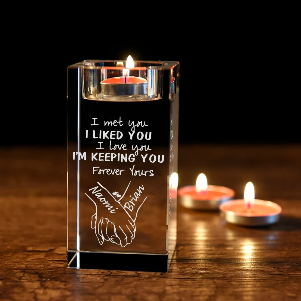 Engraved clear crystal tea light candle holder glowing in a dim romantic dinner setting beside small candles.
