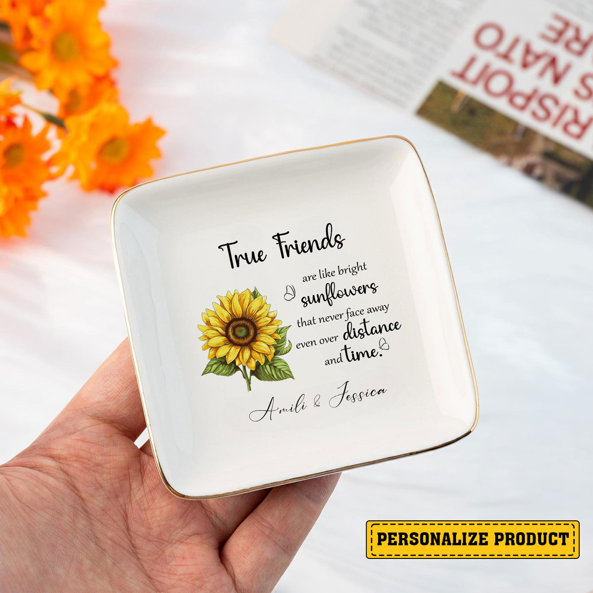Hand holding square ceramic jewelry dish with gold rim, sunflower graphic, friendship quote, and custom names.