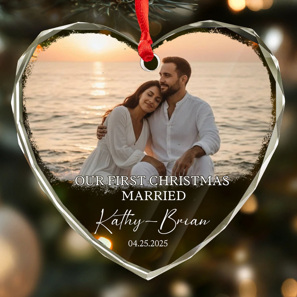 Close-up of a personalized heart glass ornament showing a couple by the sea, printed text 'OUR FIRST CHRISTMAS MARRIED'