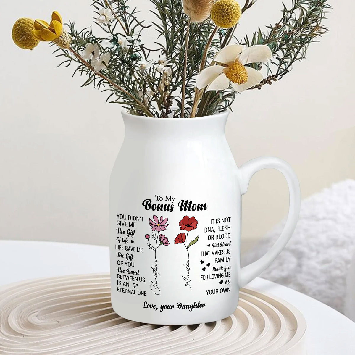 White ceramic flower vase filled with dried flowers sitting on a round wooden tray on a white table.