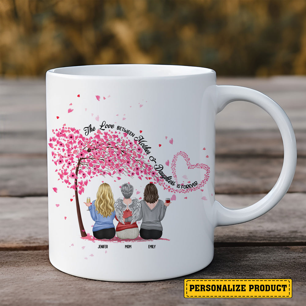 White ceramic memorial mug with a custom illustration of three women sitting under a cherry blossom tree, set on wood.