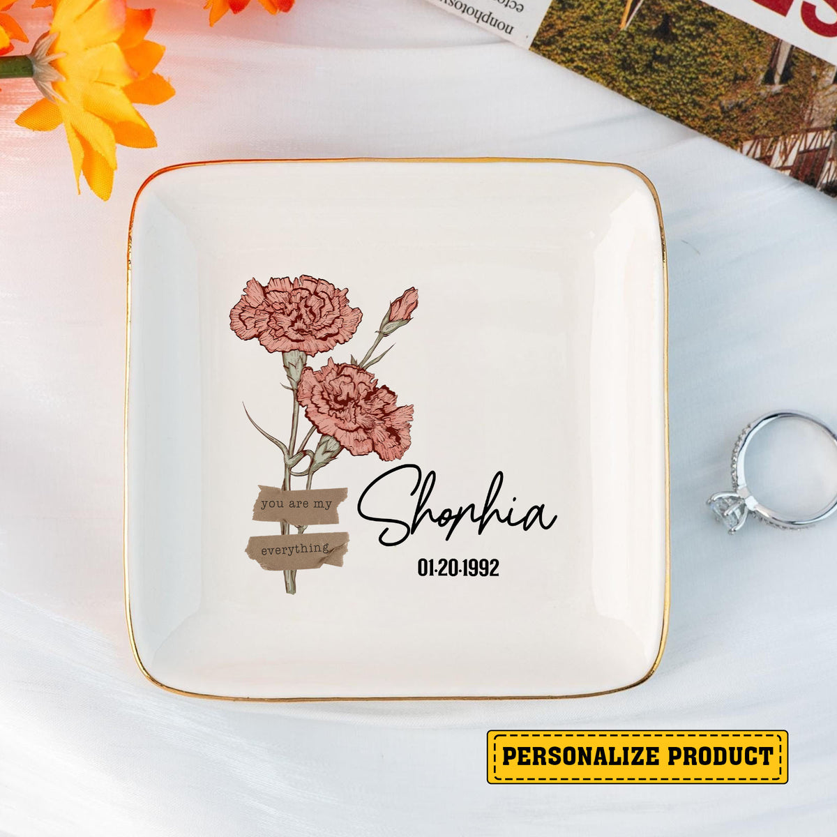 Custom jewelry dish for women featuring pink carnations and gold rim next to a sparkling ring.