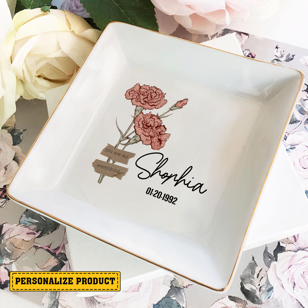 Square ceramic trinket dish with floral illustration and gold edges resting on floral stationery.