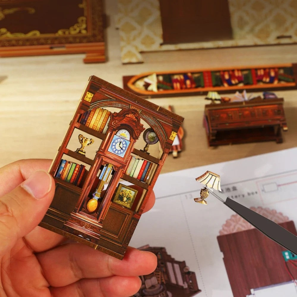 Hands using tweezers to assemble a tiny wooden clock and lamp component for the DIY miniature craft kit for adults, with