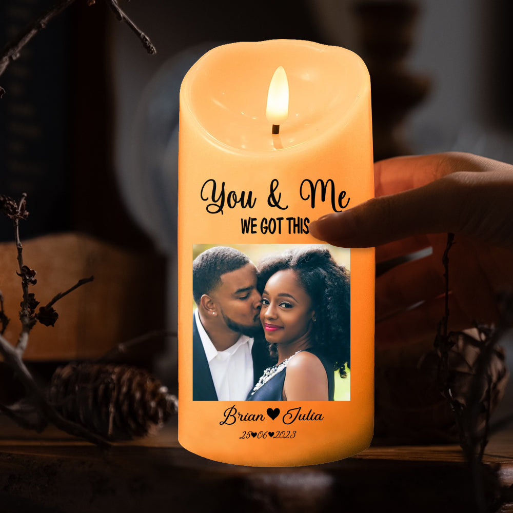 Hand holding amber LED pillar candle with custom couple photo, names, and date, featuring a flickering teardrop flame.