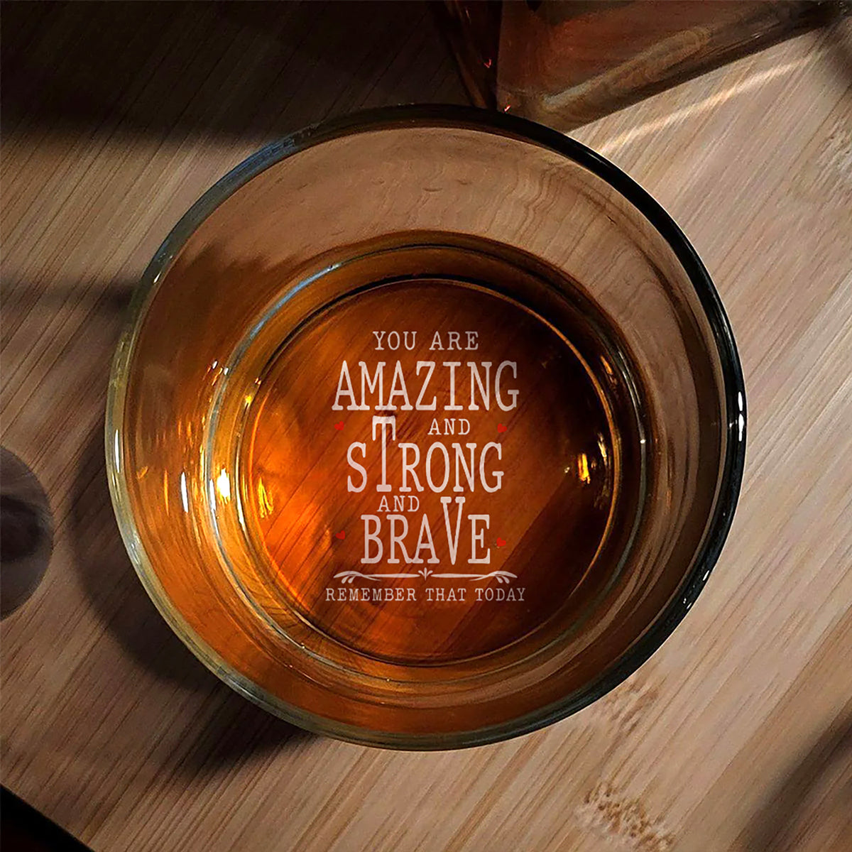 Top-down view of an 11oz clear glass whiskey tumbler resting on a wooden surface, showing the inspirational engraved quote