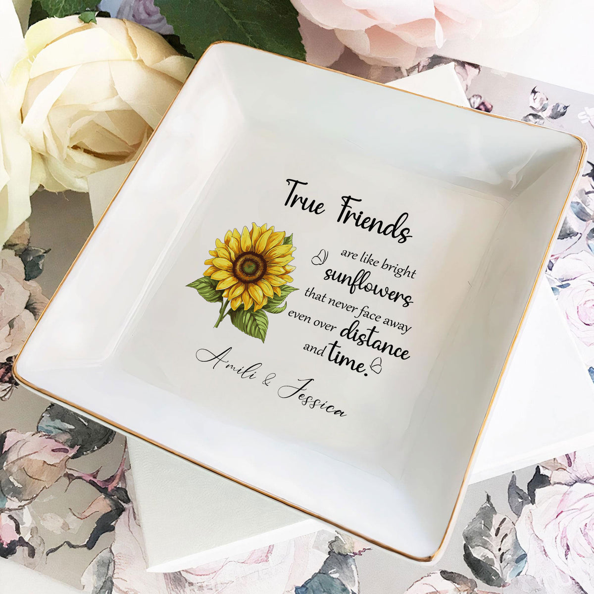 Square glazed ceramic ring dish with sunflower graphic and custom names atop floral patterned paper.