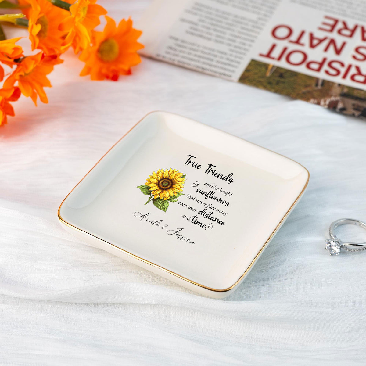 White square ceramic ring dish with gold rim, sunflower graphic, friendship quote, and custom names on a white surface.