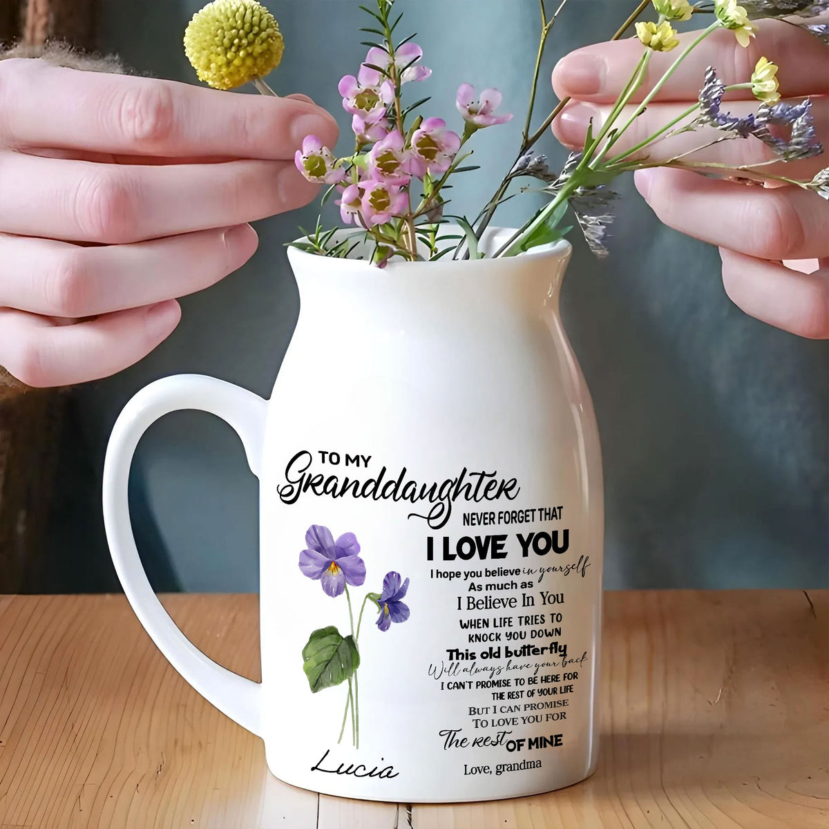 Hands arranging pink and yellow flowers into the custom ceramic vase for granddaughter on a wooden table.