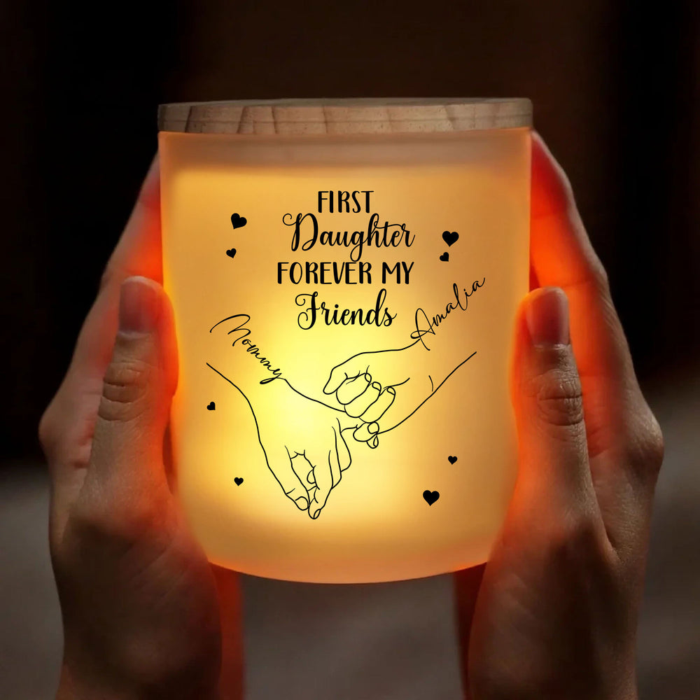Pair of hands holding glowing custom glass jar with LED candle on dark background.