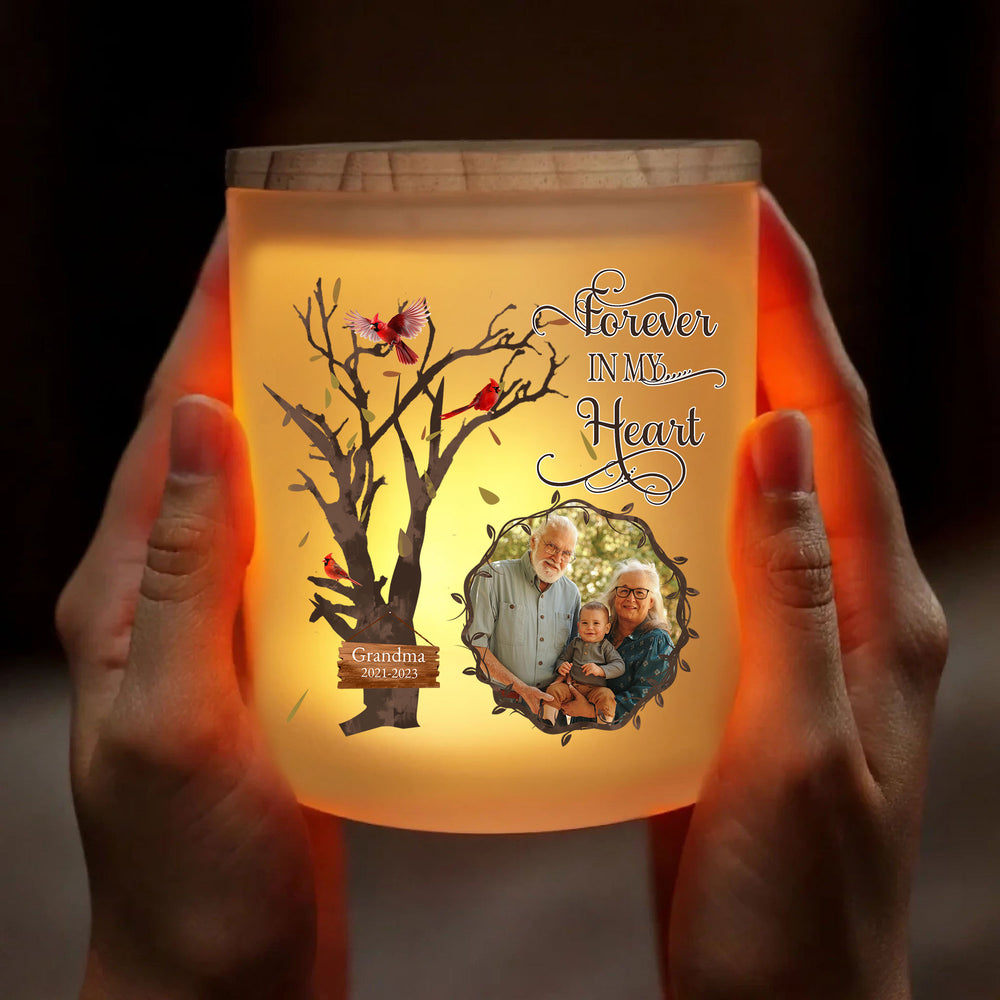 Hands holding the glowing glass jar memorial light with custom family photo and cardinal tree artwork.