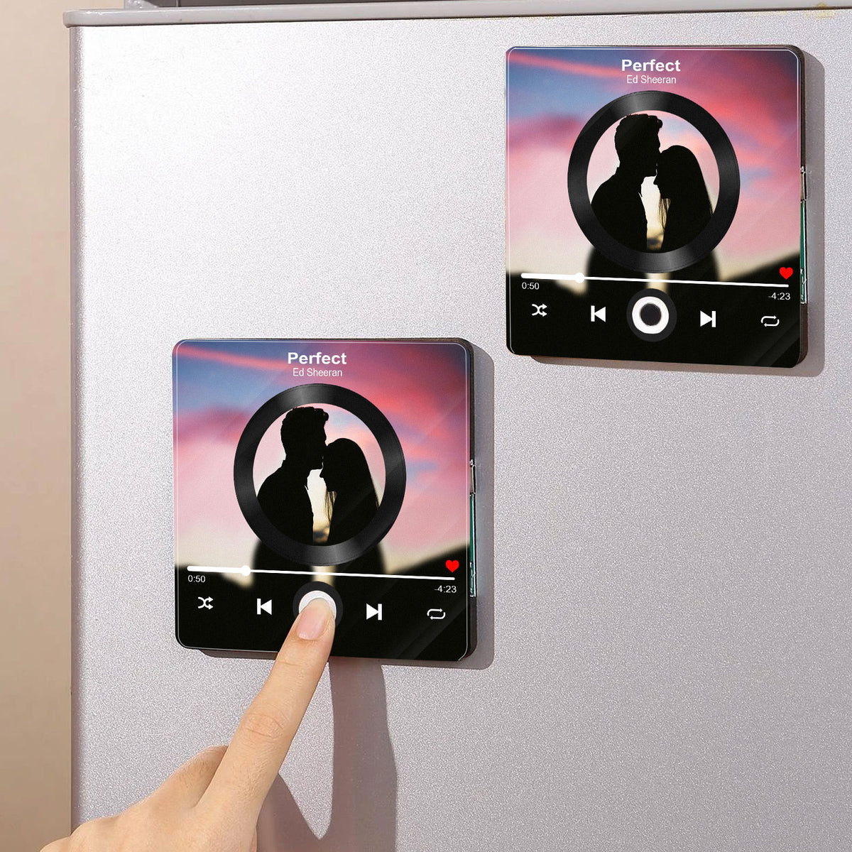 Two custom photo refrigerator magnets attached to a metal fridge, featuring couple pictures and music player design