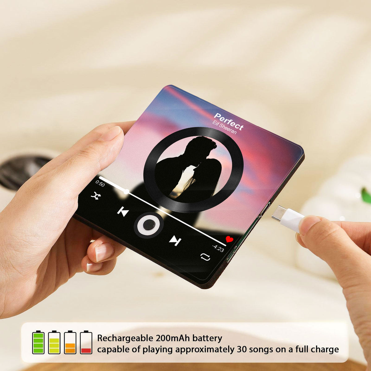 Hands charging a personalized music player fridge magnet with a white USB-C cable on a light surface