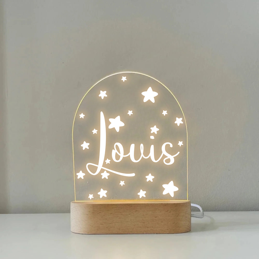 Custom printed night lamp on light wooden oval base against a neutral wall, glowing with warm LED light and star patterns.