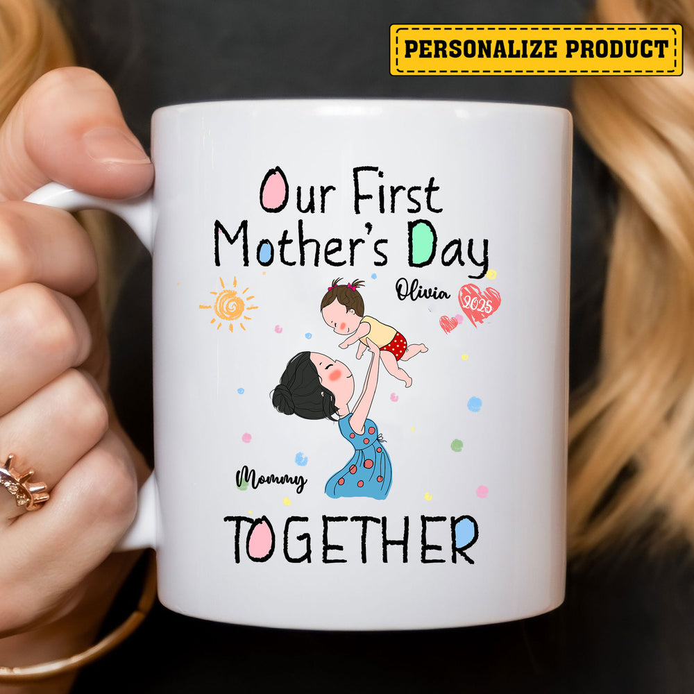 Close-up of a white ceramic mug held by a hand, featuring a custom mom and baby design with text reading Our First Mother's