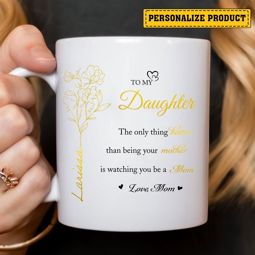 Close-up of white personalized ceramic coffee mug held by hands, featuring gold text and floral illustration.