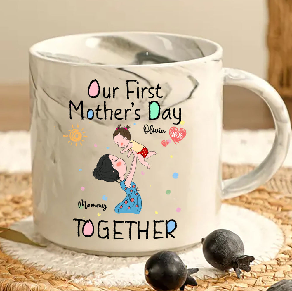 White marble mug featuring custom Our First Mother's Day design on woven placemat next to two black berries.
